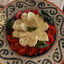 A close-up shot of a Caprese salad presented on a decorative plate, featuring slices of mozzarella, red tomatoes, and fresh basil leaves, topped with dried herbs.