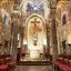 An interior shot of an old, brick-walled church or chapel, featuring a central altar with a crucifix above it, flanked by large stone columns and rows of wooden pews.