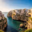 
        Create a visually captivating cover image which encompasses Perched dramatically on limestone cliffs, this idyllic town offers a breathtaking blend of stunning views, whitewashed streets, and crystalline waters. Immerse yourself in the local culture and savor the exquisite flavors of traditional Apulian cuisine. Explore hidden coves and witness unforgettable sunsets over the Adriatic Sea..
        Highlight the central location of Polignano a Mare. Focus on iconic landmarks, hidden gems, and the unique atmosphere of the location as described. Depict the image during spring.