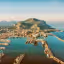 An aerial view of a bustling port city nestled at the base of a large mountain, with numerous ships, docks, and urban sprawl extending towards the distant horizon.