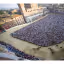 This image captures the excitement of the Palio di Siena from an aerial perspective, providing a comprehensive view of the horse race, the massive crowd, and the historic Piazza del Campo. The natural lighting is excellent, contributing to vibrant and accurate colors. Key elements like the horses and the track are sharp, and the overall photo-realism is high, effectively conveying the scale and atmosphere of the event.