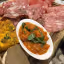 A close-up shot of an appetizer platter featuring various items such as sliced charcuterie, a yellow frittata-like dish, a bowl of red sauce, and bread with spread. The composition fills the frame, presenting a rich culinary display.