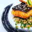 A well-composed and professionally taken close-up of a salmon dish with lentils and an artistic plate design. The lighting is excellent, highlighting the textures and vibrant colors of the food. The main elements, the salmon and lentils, are sharp and in focus, contributing to the overall photo-realistic quality. The colors appear accurate, making the dish look appetizing.