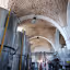 An interior view of a winery, featuring large metal fermentation tanks and an ornate arched brick ceiling.