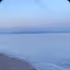 An outdoor shot of a pebble beach next to the sea with distant mountains under a muted sky.
