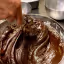 The image effectively captures the rich texture and glossy appearance of chocolate batter, benefiting from excellent photo-realism and sharp focus on the key elements. The composition is strong, drawing attention to the dynamic swirls of the batter. While generally well-lit, some of the darker areas could benefit from slightly more illumination to reveal further detail.