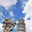 An editorial style image showcasing the Leaning Tower of Pisa in the background, framed by a classical marble sculpture featuring cherubs in the foreground. The sky is blue with scattered white clouds.