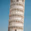 The image prominently features the Leaning Tower of Pisa against a clear blue sky, showcasing its iconic tilt and intricate architectural details. The composition is strong, focusing entirely on the tower without distractions, and the lighting is bright and even, highlighting the texture of the stone.