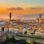 A beautiful panoramic view of Florence, Italy, captured during sunset or golden hour, featuring the iconic Duomo and Giotto's Bell Tower, with the Arno River in the foreground. The warm light bathes the historic buildings, creating a picturesque and vibrant scene.