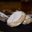 A close-up shot of several sugar-dusted cookies, with one prominently in focus in the foreground on a dark surface. The background shows more blurred cookies.