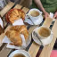 An overhead shot of a breakfast setting featuring three cups of coffee and several croissants on a rustic wooden table, with hands subtly visible in the background.