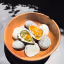 A professionally taken close-up image featuring two gourmet oysters, one adorned with green oil and the other with an orange sauce, presented artfully on natural stones inside a wooden bowl. The image captures the fresh and appetizing appearance of the dish.