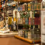 The image demonstrates strong composition with effective shallow depth of field, drawing attention to the foreground products. Key elements, such as the packaged goods and bottles, are sharp and accurately in focus. The lighting is natural and generally even, supporting the photo-realistic quality and accurate color representation. Overall, it's a high-quality editorial image of a shop interior.